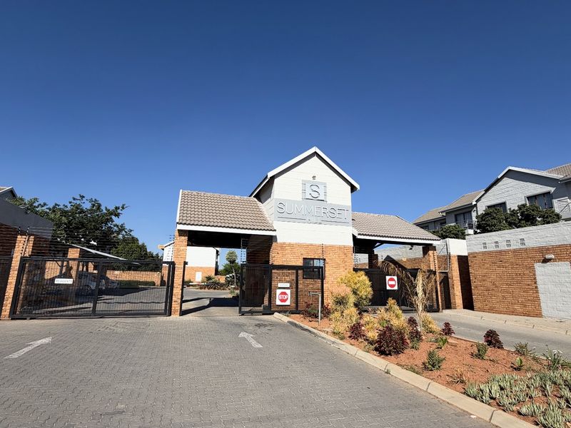 The secure entrance gate and guardhouse of the Summerset Hill townhouse complex, featuring brick construction, paved driveway, and perimeter security fencing.