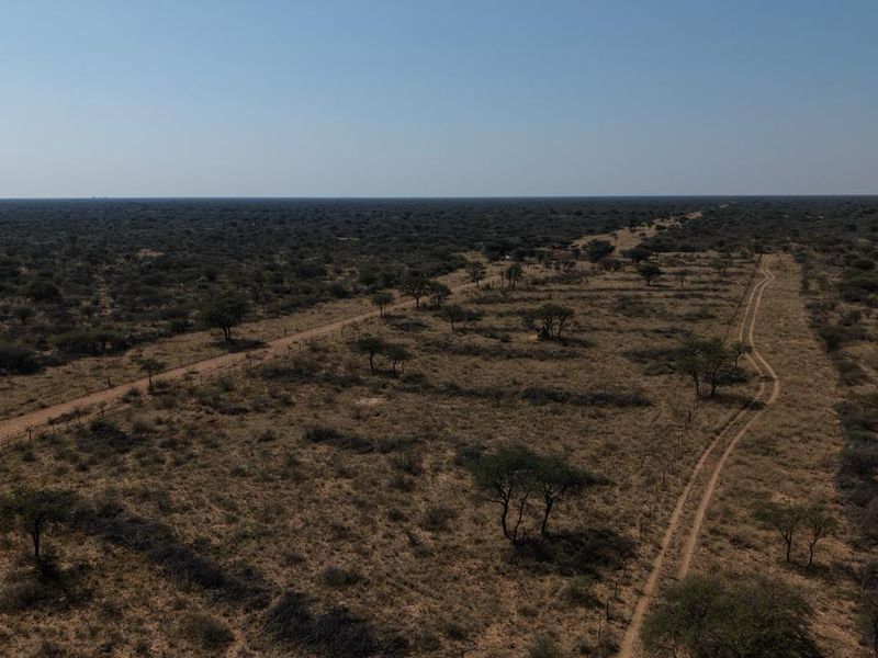 An aerial view of expansive farm land featuring natural vegetation, dirt access tracks, and perimeter fencing.