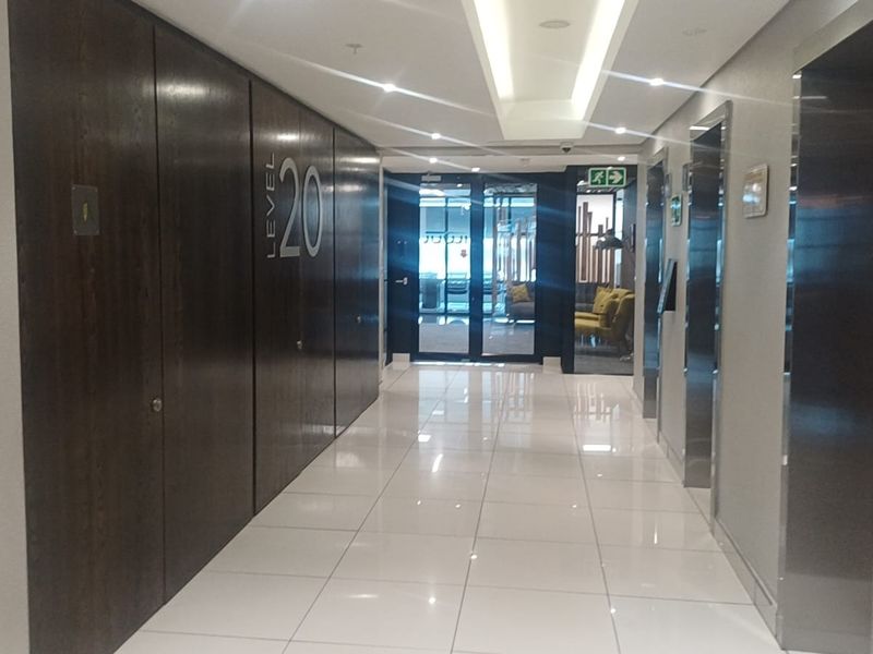A modern, well-maintained office building elevator lobby featuring polished tile flooring, recessed ceiling lighting, and dark wood paneling.