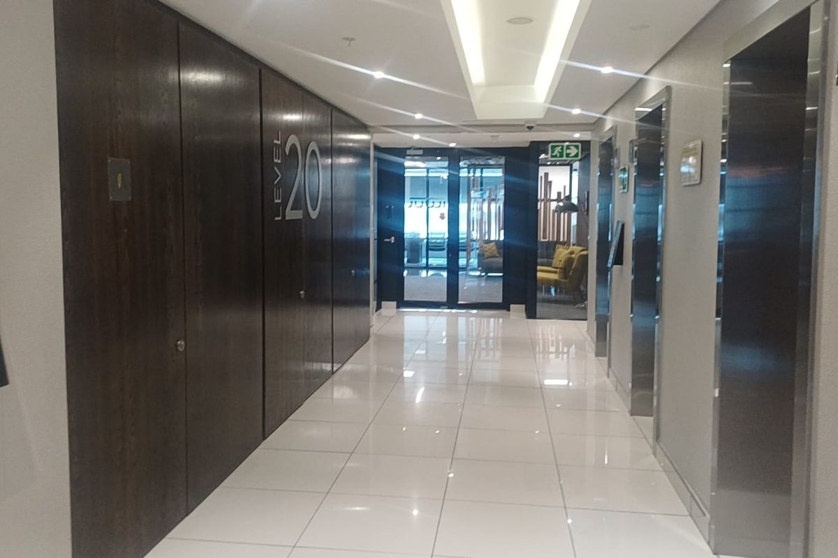 A modern, well-maintained office building elevator lobby featuring polished tile flooring, recessed ceiling lighting, and dark wood paneling.