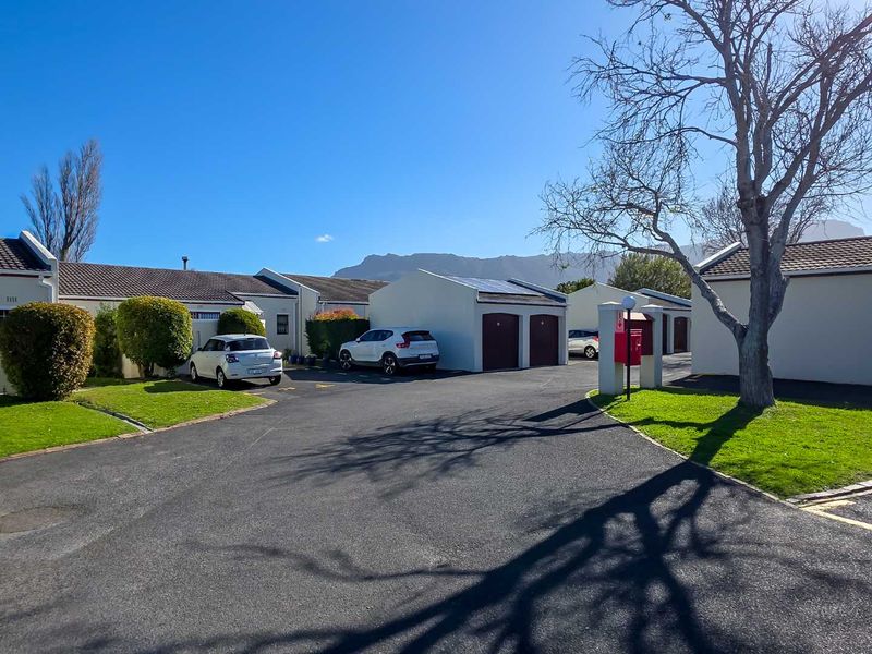 A well-maintained residential complex exterior featuring an asphalt driveway, double garage with solar panels, and manicured lawns under a clear blue sky.