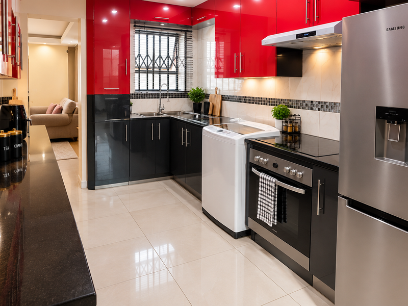 Modern kitchen featuring high-gloss red and black cabinetry, granite countertops, integrated appliances, and polished tile flooring with a view into the living area.