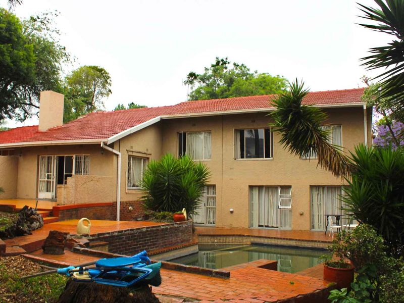 Rear view of the house featuring a swimming pool, brick patio area, and terracotta tiled roof, set within a mature garden.