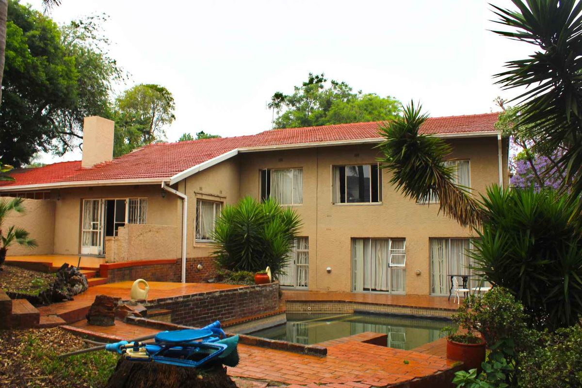 Rear view of the house featuring a swimming pool, brick patio area, and terracotta tiled roof, set within a mature garden.