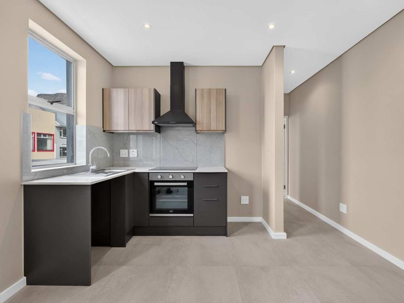 Modern kitchen featuring dark cabinetry, stone countertops, integrated oven and hob, extractor fan, and tiled flooring in a clean, minimalist space.