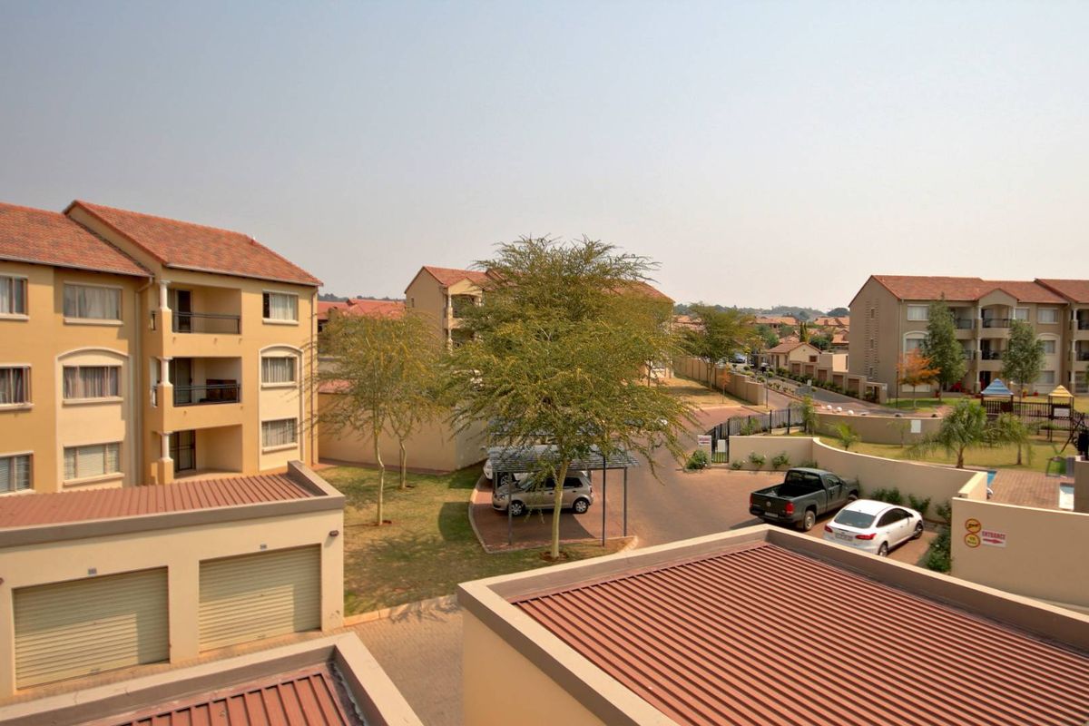 Elevated view of the apartment complex grounds, featuring multiple residential buildings, paved driveways, covered parking areas, and landscaped communal spaces.