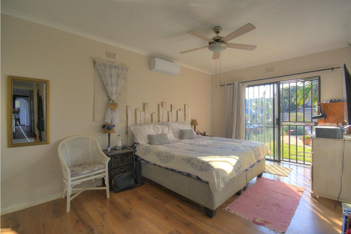 A bedroom featuring laminate flooring, a ceiling fan, a wall-mounted air conditioner, and sliding glass doors providing access to the garden.