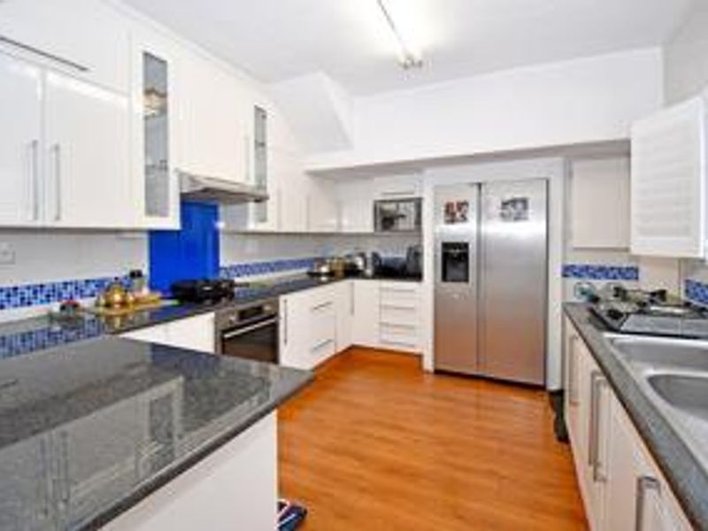 A functional kitchen featuring granite countertops, white cabinetry, a built-in oven, extractor fan, and a double stainless steel sink with a tiled backsplash.