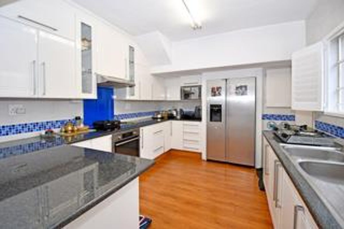 A functional kitchen featuring granite countertops, white cabinetry, a built-in oven, extractor fan, and a double stainless steel sink with a tiled backsplash.