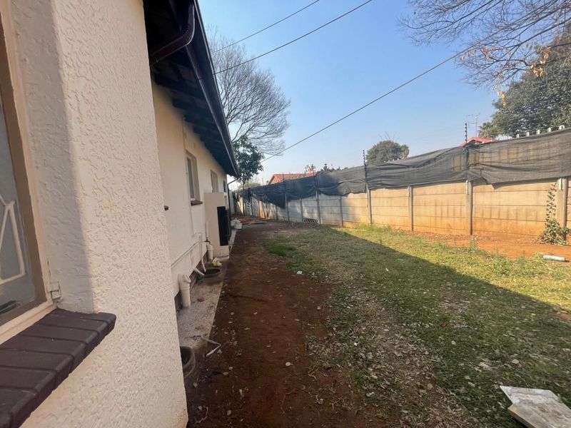 A side view of the property showing the exterior wall, precast boundary fencing with electric security, and an unlandscaped garden area.
