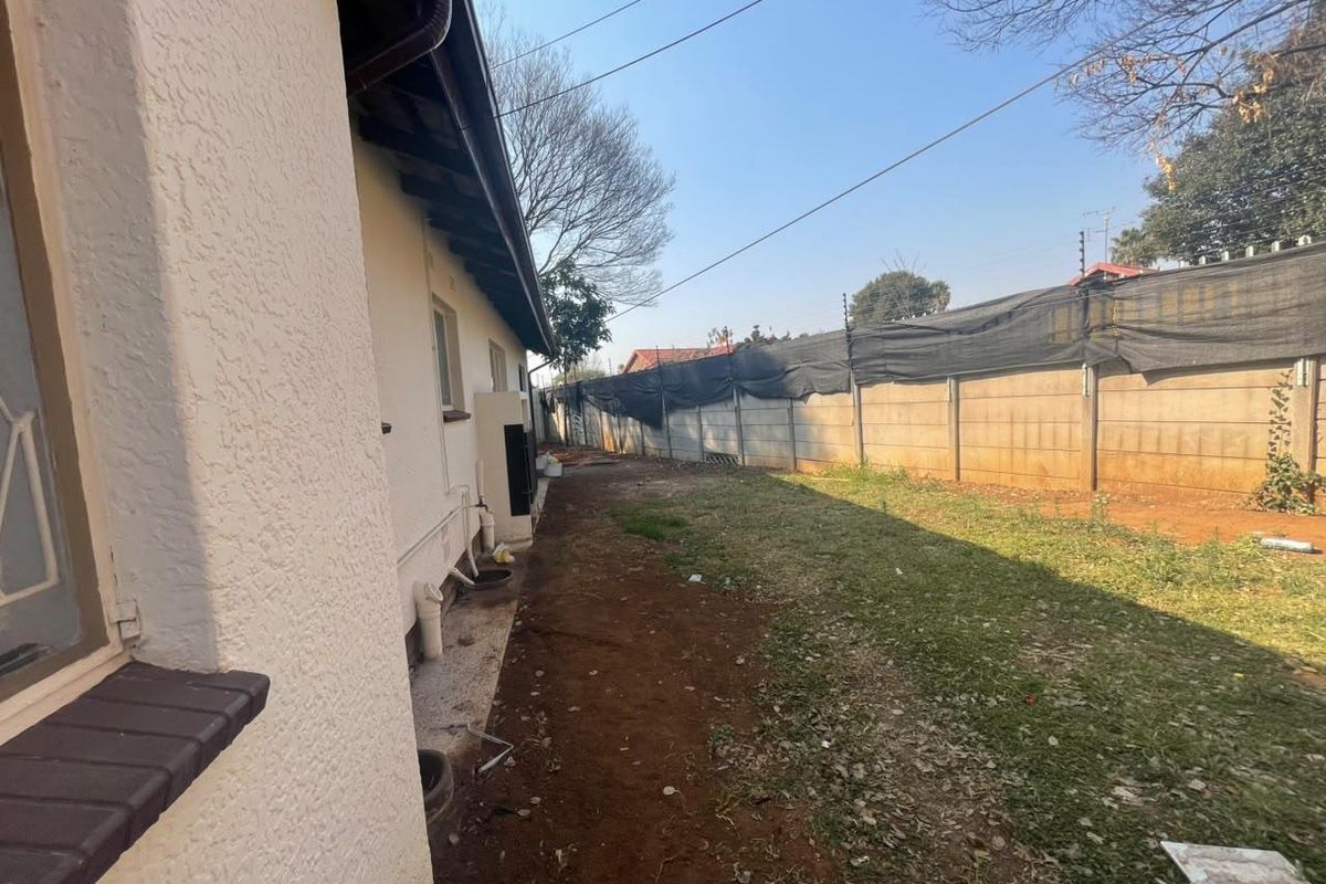 A side view of the property showing the exterior wall, precast boundary fencing with electric security, and an unlandscaped garden area.