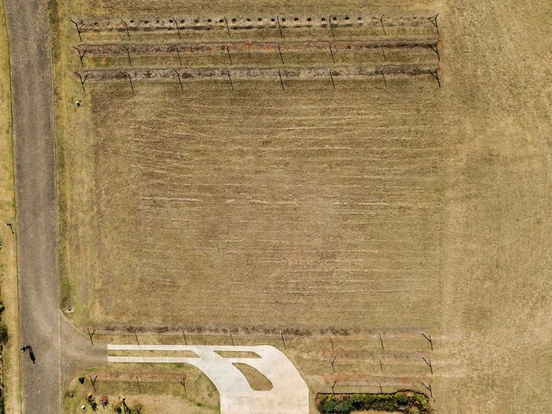 An aerial view of a vacant residential plot featuring a paved driveway entrance and perimeter fencing.