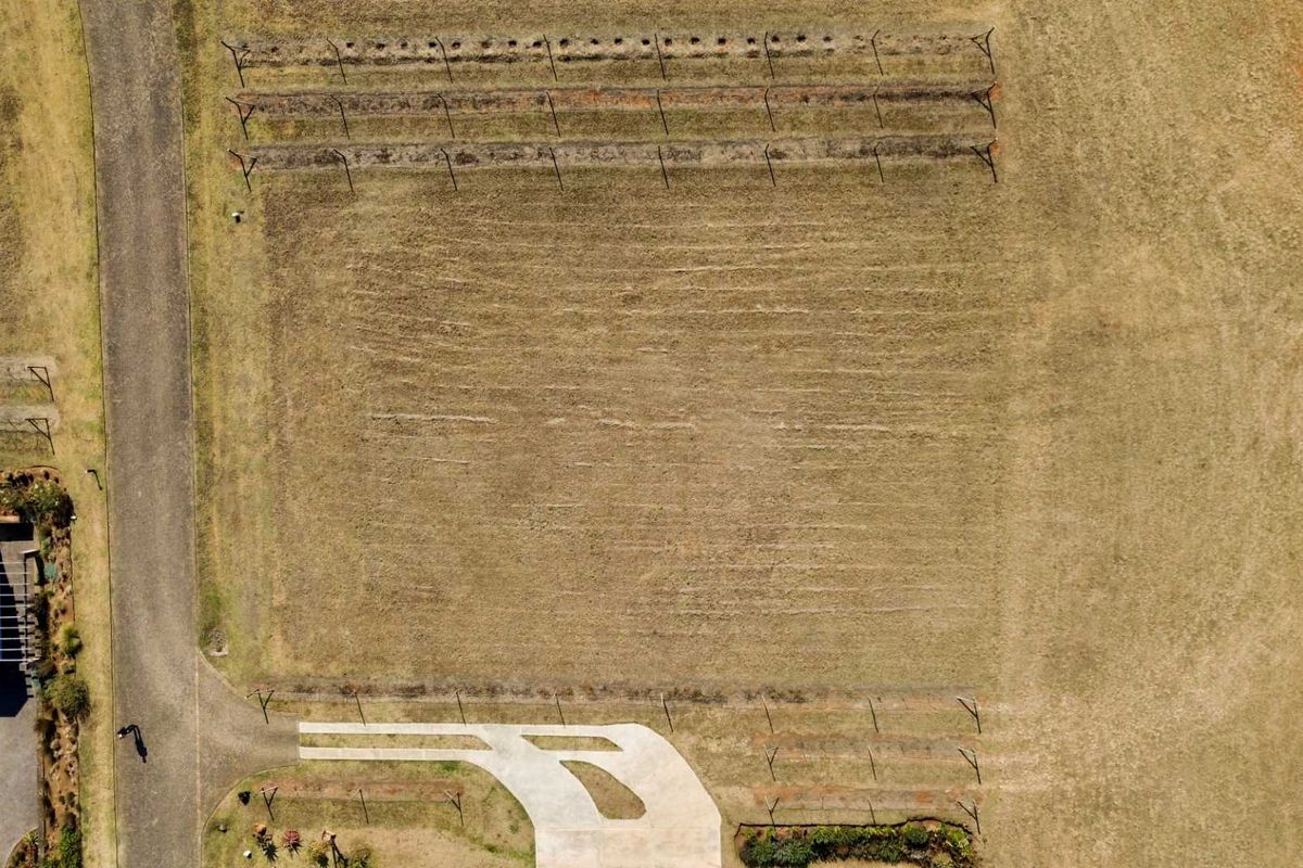 An aerial view of a vacant residential plot featuring a paved driveway entrance and perimeter fencing.