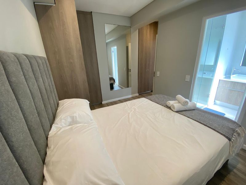 Modern bedroom featuring built-in wooden cupboards, laminate flooring, and an integrated en-suite bathroom with contemporary finishes.