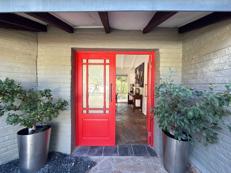 A welcoming entrance featuring a vibrant red door, stone flooring, and exposed timber ceiling beams under a covered porch area.