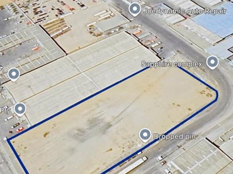 An aerial view of a vacant industrial plot located within a commercial complex, showing surrounding infrastructure and road access.