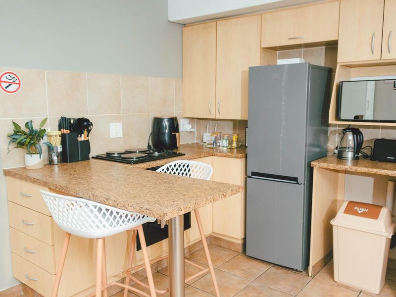 A compact kitchen featuring light wood-finish cabinetry, granite-look laminate countertops, ceramic tile backsplash, and tiled flooring with an integrated breakfast bar.