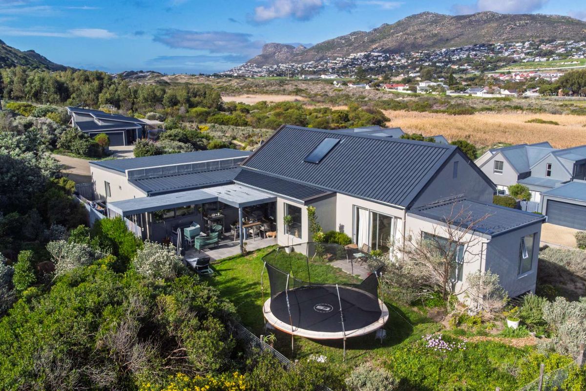 Aerial view of a modern residential property featuring a metal roof, solar heating, and a spacious covered patio overlooking a landscaped garden.