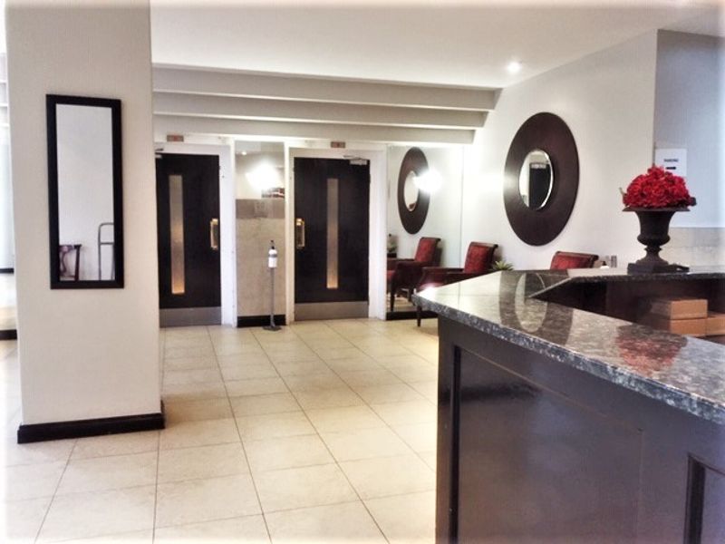 A well-maintained apartment building entrance lobby featuring a reception desk, tiled flooring, and modern double door access.
