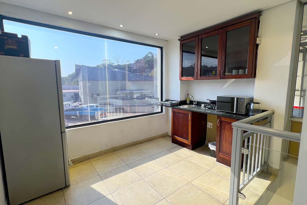 Compact kitchen area featuring dark wood cabinetry, granite countertops, a stainless steel sink, and large windows providing ample natural light.