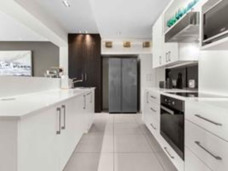 Modern kitchen featuring sleek white cabinetry, stone countertops, integrated appliances, and high-quality finishes with a clean, contemporary aesthetic.