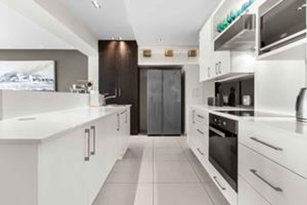 Modern kitchen featuring sleek white cabinetry, stone countertops, integrated appliances, and high-quality finishes with a clean, contemporary aesthetic.