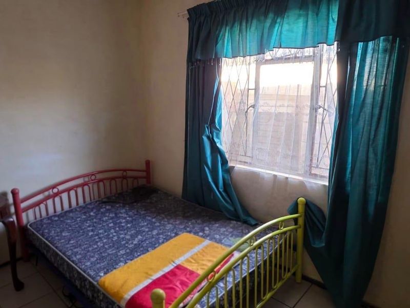 A bedroom featuring tiled flooring and a window fitted with security bars, requiring cosmetic updates to the walls.