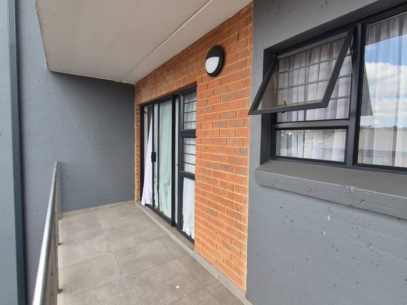 A covered balcony featuring tiled flooring, brick and rendered wall finishes, and black-framed windows and sliding doors.