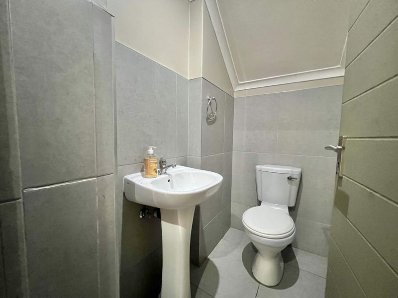 A compact guest bathroom featuring a pedestal basin, toilet, and neutral grey wall and floor tiling.