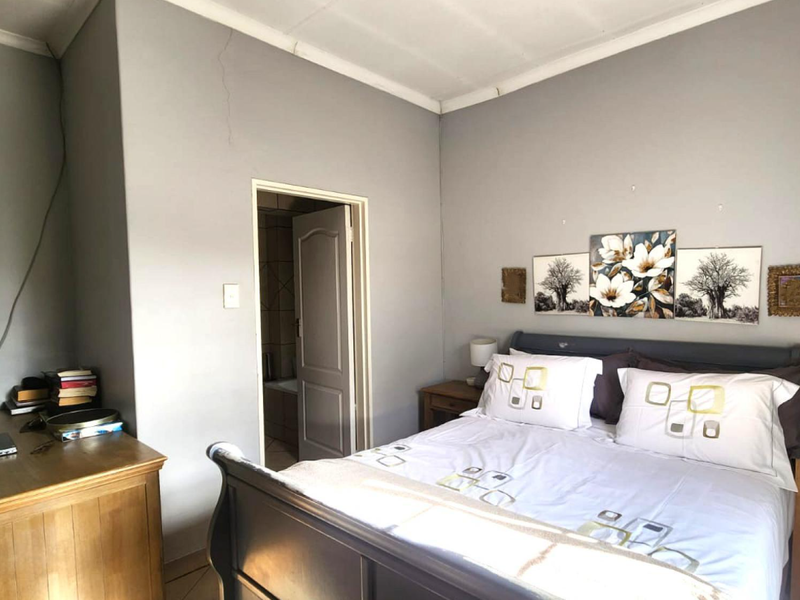 A bedroom featuring a coved ceiling and an adjoining bathroom entrance, showing a visible wall crack requiring maintenance.