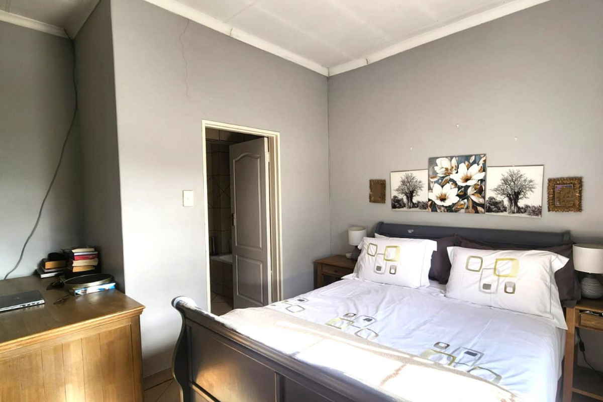 A bedroom featuring a coved ceiling and an adjoining bathroom entrance, showing a visible wall crack requiring maintenance.