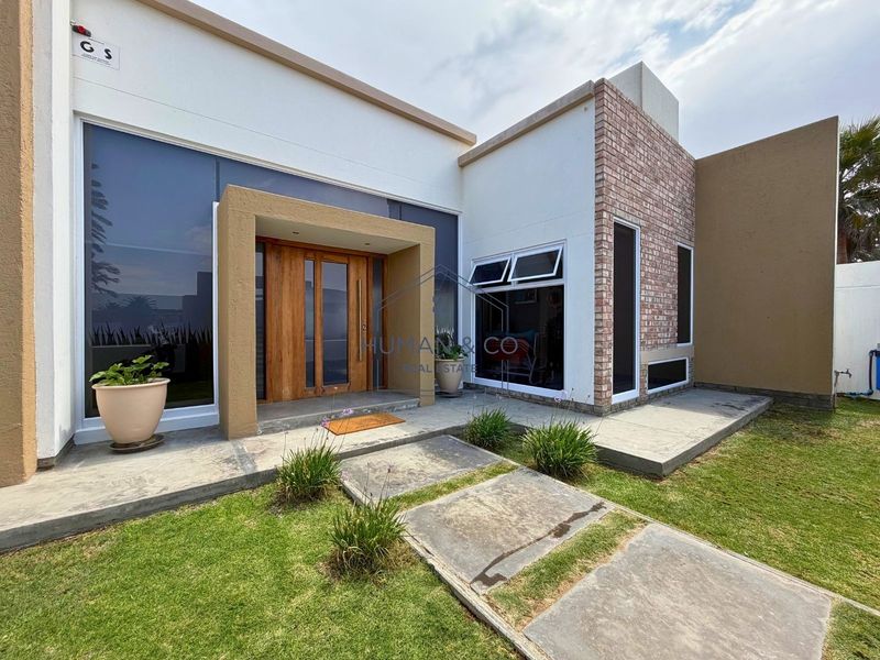Modern front entrance featuring a striking wooden pivot door, large glass windows, and a combination of white render and exposed brick finishes.