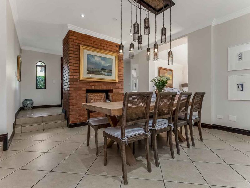A well-maintained dining area featuring a prominent exposed brick fireplace, tiled flooring, and elegant pendant lighting, creating a warm and inviting atmosphere.