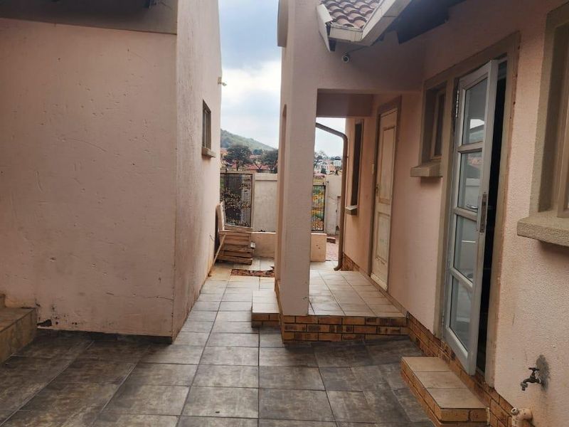 A paved rear courtyard area featuring tiled flooring, security gates, and external access points, providing a functional outdoor space between building sections.