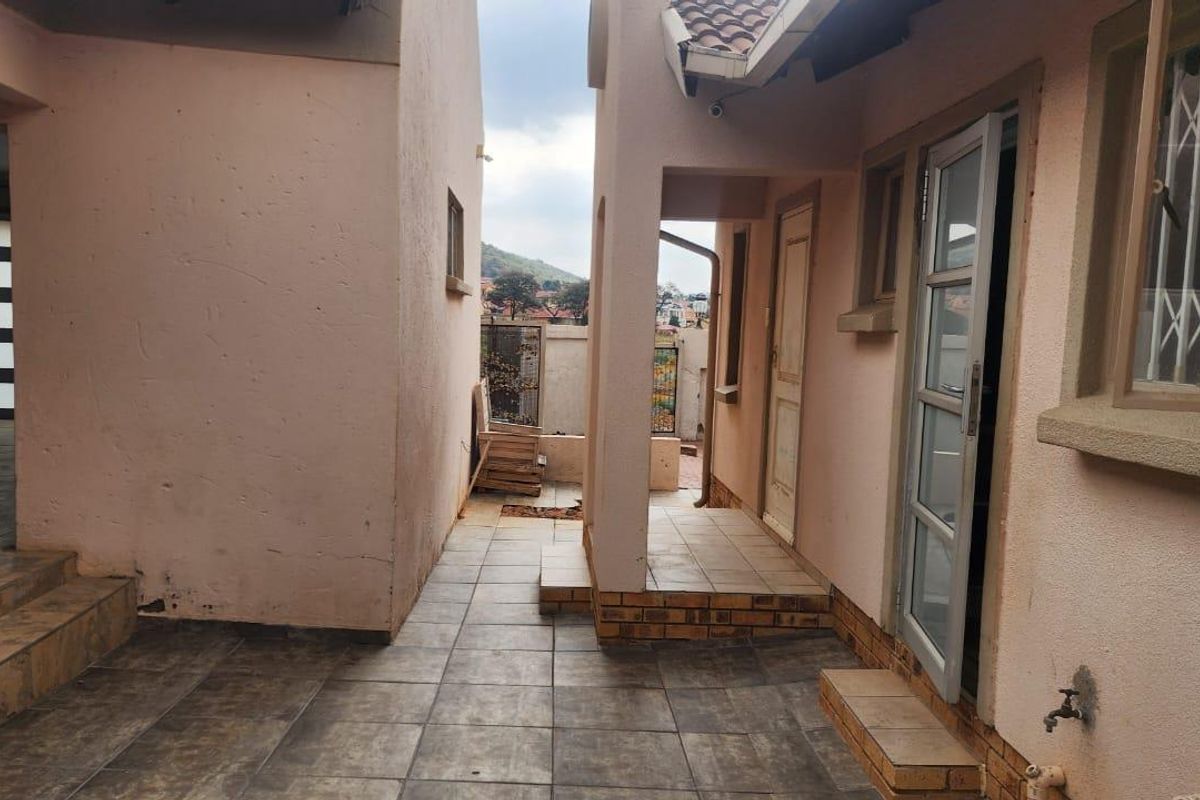 A paved rear courtyard area featuring tiled flooring, security gates, and external access points, providing a functional outdoor space between building sections.
