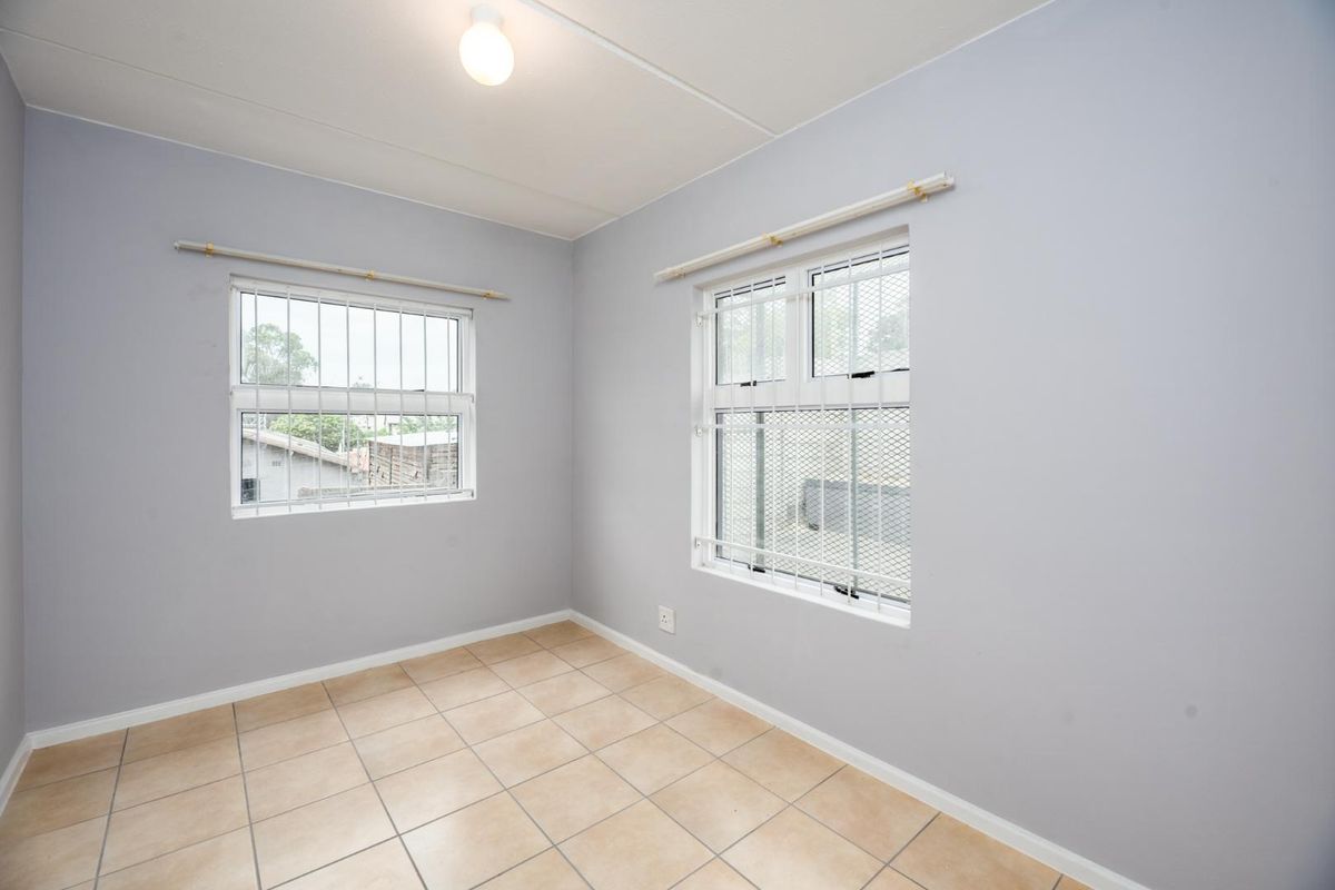 A bright, empty bedroom featuring neutral grey walls, tiled flooring, and security bars on the windows.