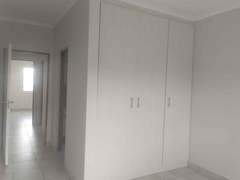 A clean, empty bedroom featuring neutral tiled flooring, white walls, and a built-in wardrobe with modern finishes.