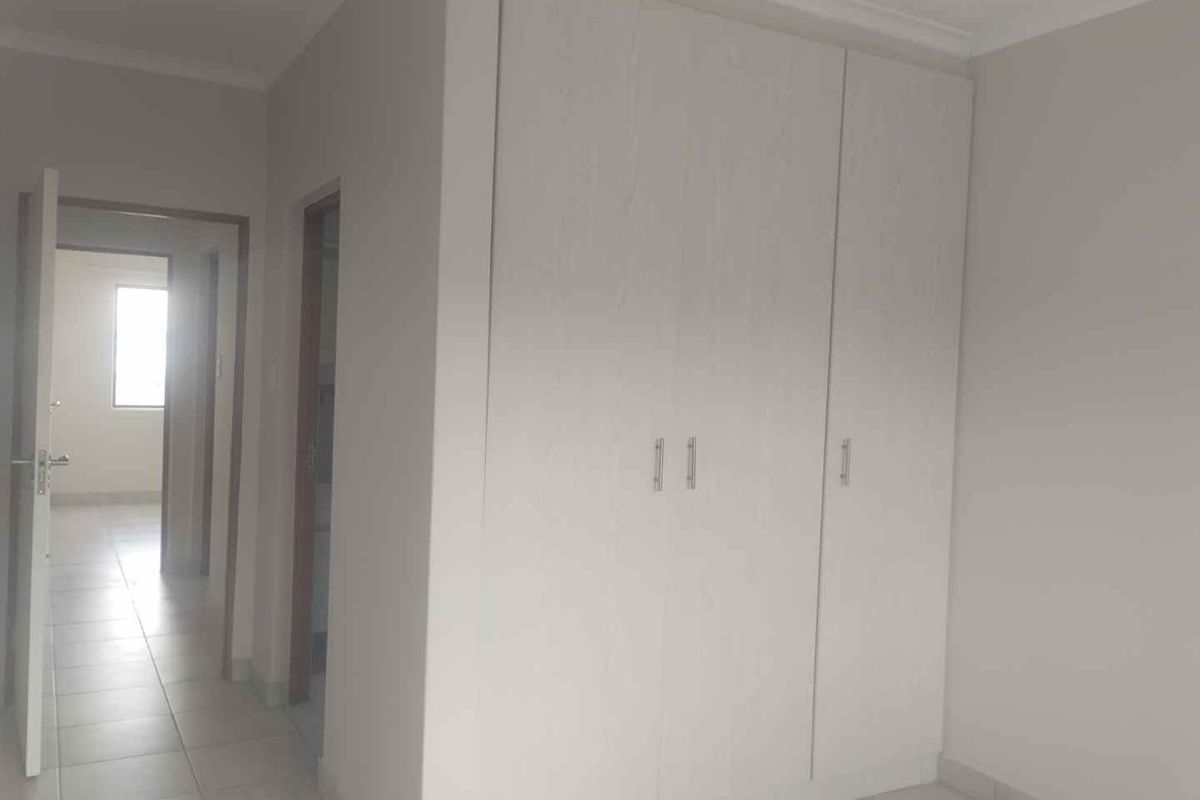 A clean, empty bedroom featuring neutral tiled flooring, white walls, and a built-in wardrobe with modern finishes.