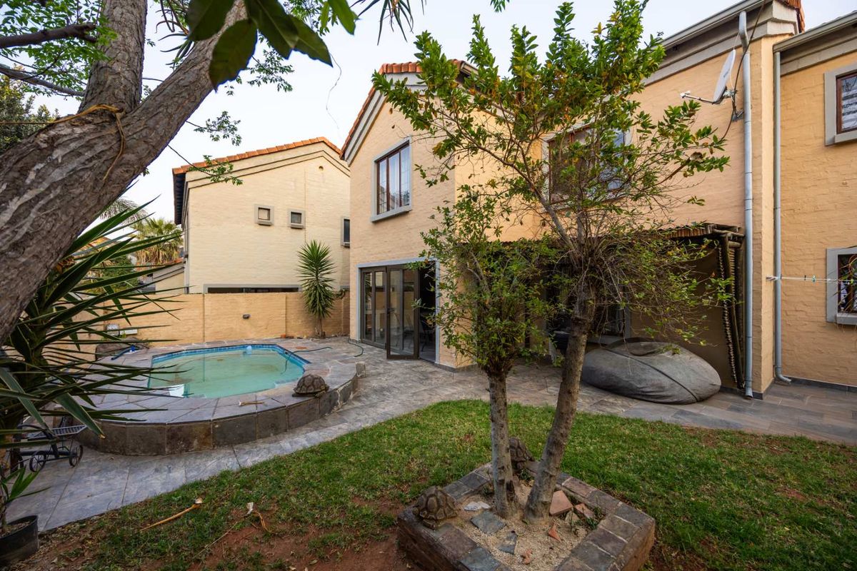 Rear exterior view featuring a swimming pool, paved patio area, and landscaped garden with established trees against the house facade.
