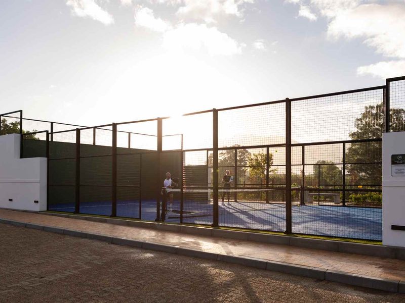 A well-maintained outdoor padel court featuring modern fencing and blue synthetic surfacing, situated within a residential estate setting.