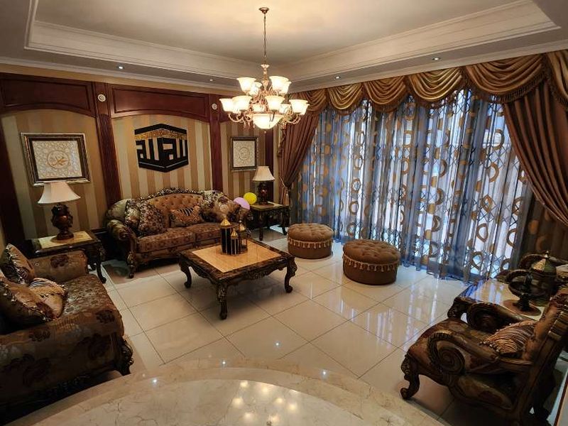 Spacious living room featuring elegant tiled flooring, decorative wall paneling, and a sophisticated recessed ceiling with integrated lighting.