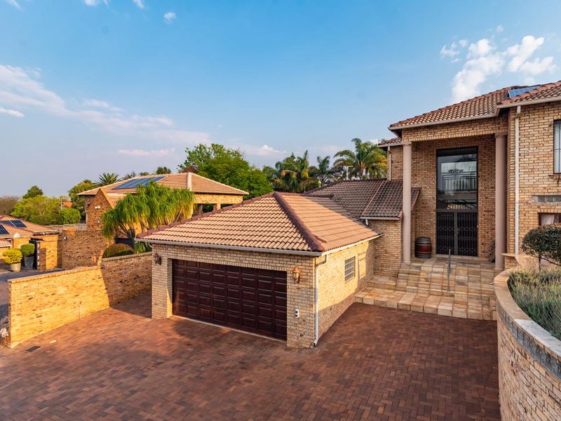 A well-maintained face brick residence featuring a paved driveway, double garage, solar panels, and an elevated entrance with stone steps.