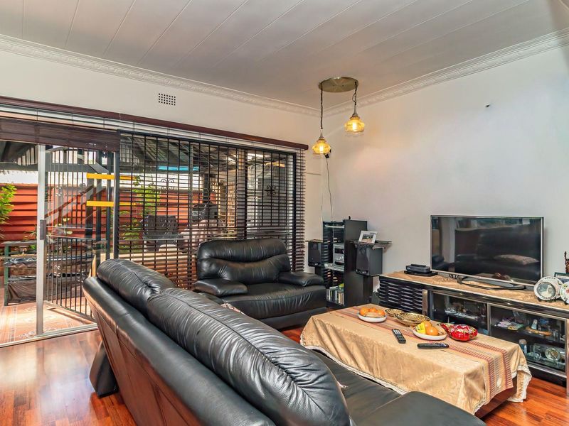 A comfortable living room featuring timber flooring, decorative ceiling cornices, and a large sliding glass door providing access to the outdoor patio area.