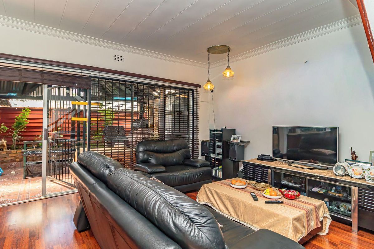 A comfortable living room featuring timber flooring, decorative ceiling cornices, and a large sliding glass door providing access to the outdoor patio area.