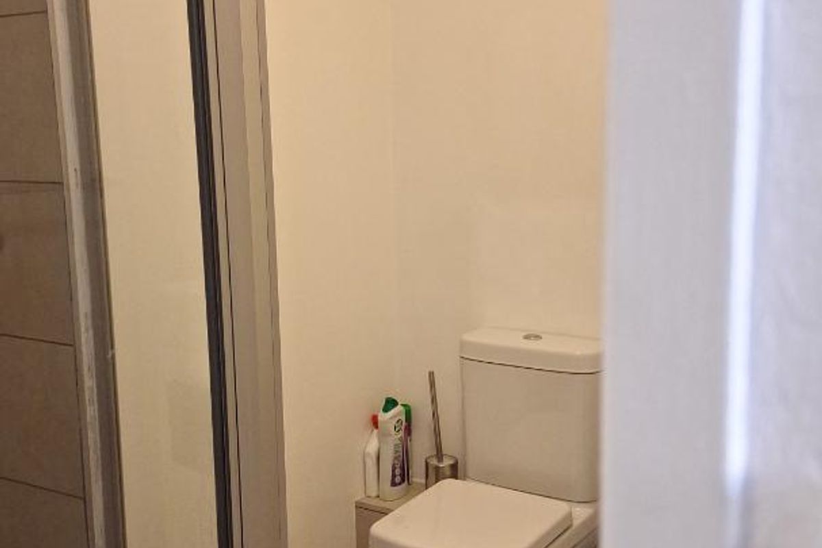 A functional bathroom featuring a glass-enclosed shower and a standard toilet with tiled flooring.