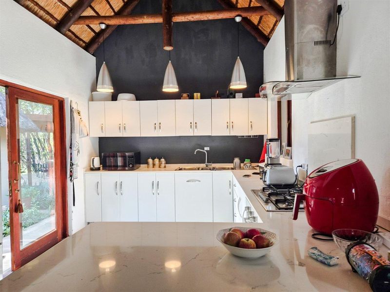 Modern kitchen featuring white cabinetry, stone countertops, gas hob, and stainless steel extractor fan, set under a high-vaulted thatched ceiling with exposed timber rafters.