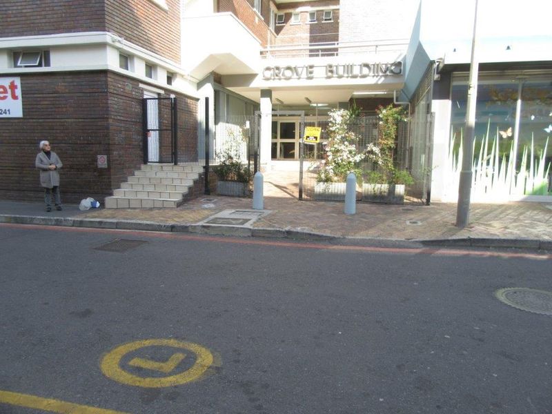 Street-level view of the Grove Building entrance, featuring a brick facade, paved access area, and security gate.