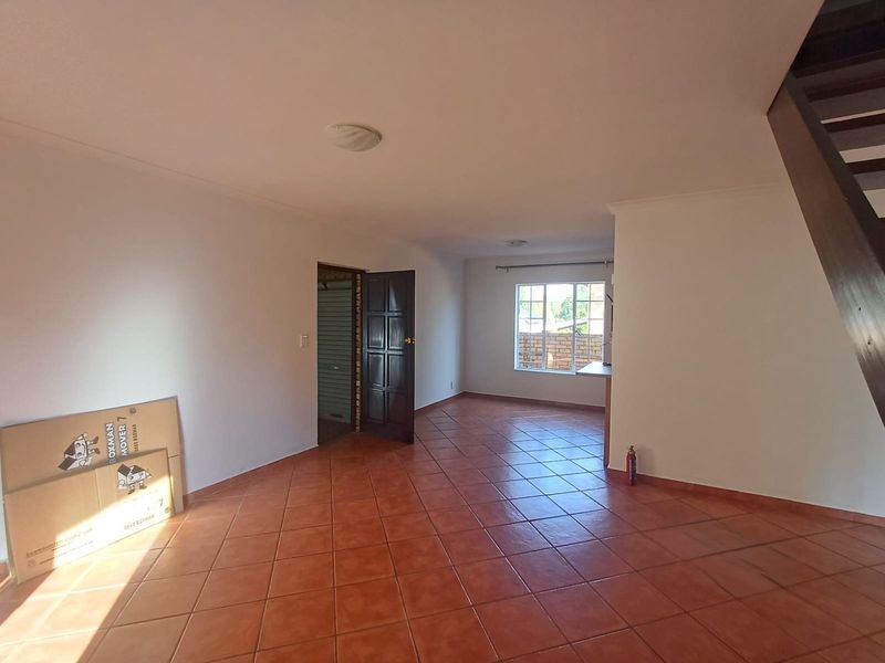 An empty, open-plan living area featuring terracotta-style floor tiles, a staircase, and neutral walls, offering a blank canvas for interior design.