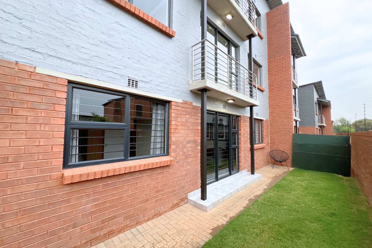 Rear view of the apartment building featuring a brick facade, ground floor patio area, and a small private garden space.