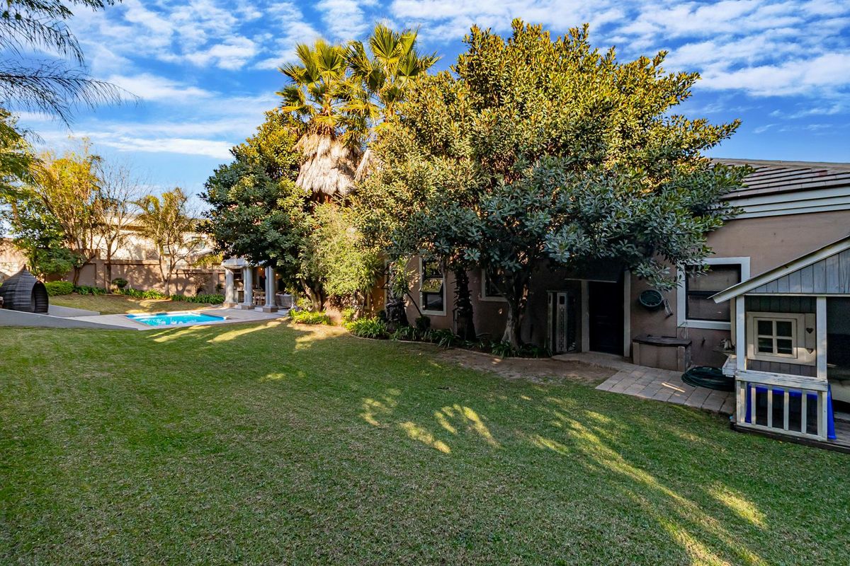 Spacious rear garden featuring a well-maintained lawn, mature trees, a swimming pool, and a paved patio area suitable for outdoor relaxation.